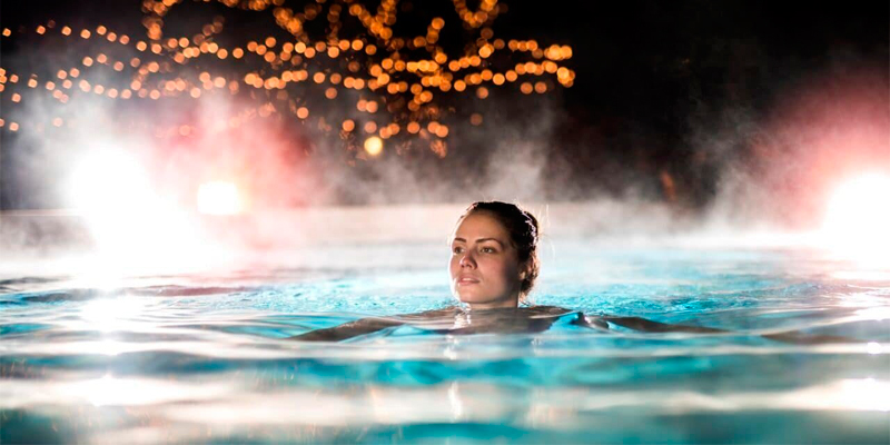 mujer nadando en piscina con calentamiento mediante bomba de calor con tecnología inverter, por la noche